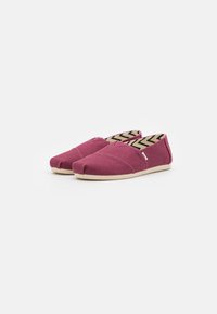 Burgundy slip-on shoes made of textured fabric with a cream rubber sole and patterned interior featuring a black zigzag design.