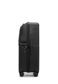 Valise rigide noire avec des rainures verticales, un cadenas à combinaison et quatre roues. Texture lisse avec un design structuré et fermeture éclair.