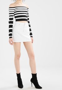 Schwarz-weißer gestreifter Off-Shoulder-Crop-Top kombiniert mit einem weißen Denim-Minirock. Das Model trägt schwarze Knöchelstiefel.