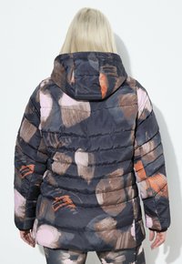 Giacca imbottita blu scuro con un motivo astratto multicolore a colpi di pennello, dotata di cappuccio e design trapuntato. Tessuto morbido e liscio.