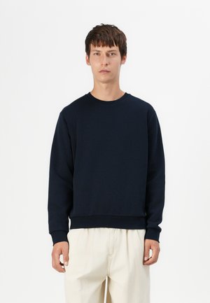 Navy crewneck sweatshirt made of soft fabric, featuring ribbed cuffs and hem, paired with light-colored loose trousers.