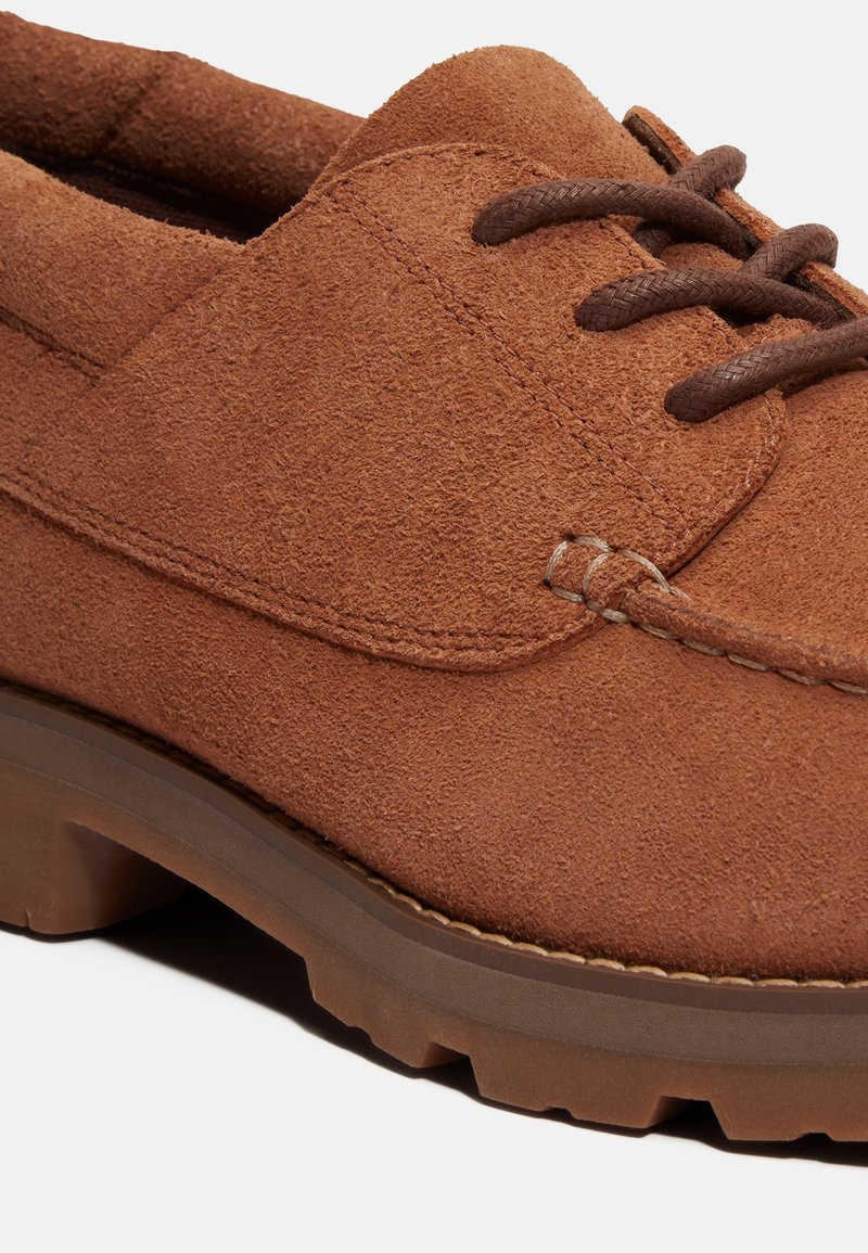 Scarpa in suede marrone con suola in gomma spessa, tomaia testurizzata e lacci marroni a contrasto. Presenta sottili dettagli di cucitura lungo i bordi.