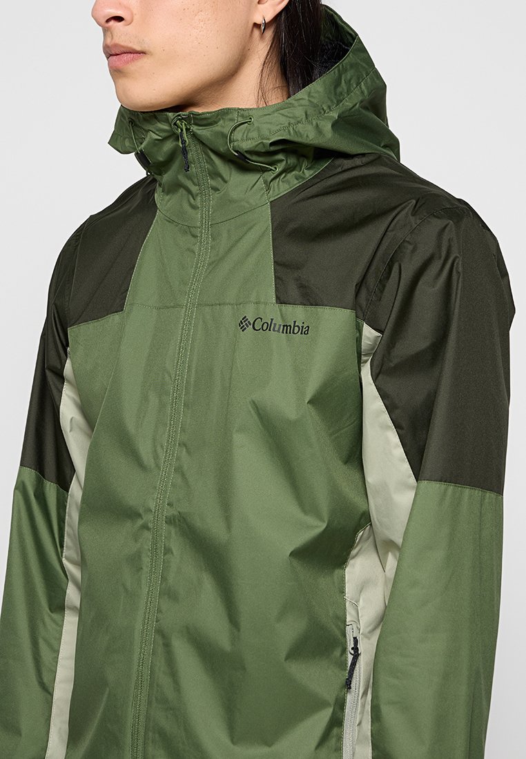 Veste imperméable verte et vert foncé avec capuche, dotée de poches latérales zippées et d'un logo sur la poitrine. Matériel léger, design épuré.