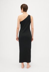Vestido maxi negro de un solo hombro con textura acanalada, silueta ajustada y largo hasta los tobillos, que muestra un diseño minimalista.