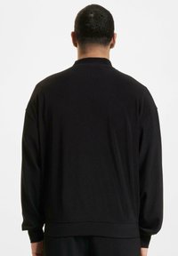 Sort langærmet top med ribbet tekstur, der har en høj krave, lav skuldersøm og en afslappet pasform. Ingen synlige logoer eller mønstre.