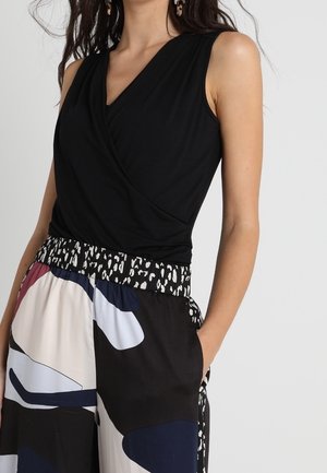 Top sans manches noir avec un design enveloppant, associé à un pantalon ample à motifs colorés présentant des formes audacieuses et une taille élastique noire.