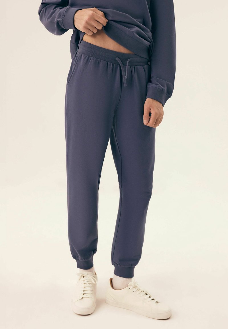 Granatowe dresy wykonane z miękkiego materiału, z elastycznym pasem, ściągaczami na kostkach i luźnym krojem. W połączeniu z białymi trampkami.