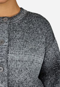 Šedý pletený cardigan se texturovaným vzorem, kulatým výstřihem a zapínáním na dva knoflíky. Výrazný přechod odstínů od tmavě šedé k světle šedé.