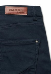 Dunkelblaue Denim-Hosen mit einem Lederlabel "GABBA", zwei Gesäßtaschen und einem metallischen Knopfakzent. Genähte Details überall.