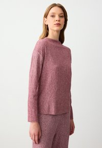 Maglione a maniche lunghe in maglia mauve testurizzata, con un colletto alto e un motivo a chevron. Abbinato a un pantalone coordinato in tessuto simile.