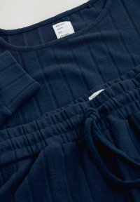 Set de loungewear bleumarin, compus dintr-un top texturat cu dungi și pantaloni cu talie elastică, prevăzuți cu șnur și etichetă care indică marca și instrucțiunile de îngrijire.