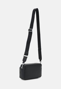 Black crossbody bag with a textured surface, rectangular shape, silver zipper, and adjustable strap featuring embossed branding.