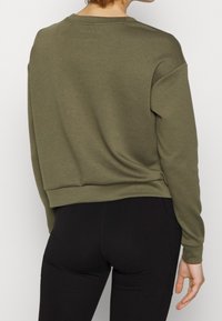 Olive green sweatshirt with a relaxed fit, crew neckline, and ribbed hem. Soft texture with minimal branding at the back. Black leggings visible.