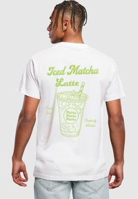 Bílý tričko s zelenou grafikou šálku označeného "Iced Matcha Latte" s kostkami ledu a mátovými lístky.