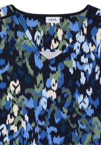 T-shirt col en V avec un motif camouflage abstrait dans des tons de bleu, vert, crème et noir, avec une étiquette de marque "CECIL" à l'intérieur du col.