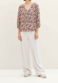 Blouse à imprimé floral avec un col en V, des manches trois-quarts et une coupe ample. Associée à un pantalon blanc à jambes larges et des chaussures à enfiler beiges.