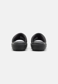 Black slide sandals with a wide upper strap, textured insole, and raised heel. Features embossed logo on the heel and patterned outsole.