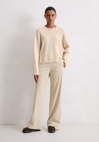 Pull en laine beige à manches longues et col rond associé à un pantalon crème à jambes larges et côtelées, avec des chaussures marron foncé. Texture lisse.