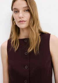 Rochie fără mâneci burgundy, cu decolteu rotund, prevăzută cu patru nasturi închiși la culoare pe partea din față. Textură netedă, design simplu.