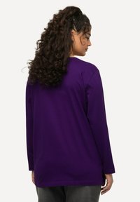 Langärmliges lila T-Shirt mit lockerer Passform, Rundhalsausschnitt und glatter Textur, ausgestattet mit Seitenschlitzen am Saum für zusätzlichen Komfort.