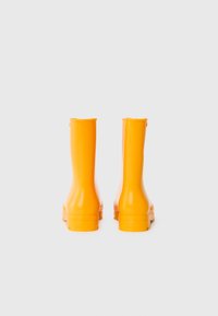 Bottes de pluie en caoutchouc jaune avec une finition brillante, design montant au genou et semelles texturées. Aucun logo ou motif visible.