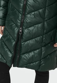 Doudoune verte avec un motif en chevron, dotée d'une fermeture éclair à l'avant et d'un tissu brillant. La texture semble lisse et rembourrée.