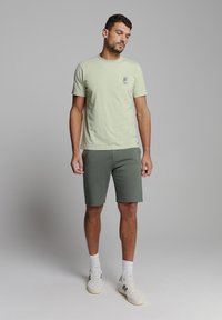 Lichtgroene katoenen t-shirt met een kleine graphic en een gestructureerde afwerking, gecombineerd met donkergroene shorts, gedragen met witte sneakers en sokken.