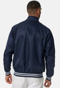 Giacca bomber blu navy con finitura liscia e lucida, polsini e orlo a coste con strisce bianche. Collo alto, design della parte posteriore semplice.