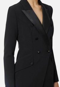 Blazer nero su misura con rever a punta in raso, design doppiopetto e bottoni decorativi. Presenta spalle strutturate e tessuto liscio.