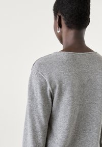 Maglione grigio a maglia con scollo ampio, caratterizzato da una finitura testurizzata. Il retro presenta cuciture minime e un fit rilassato.
