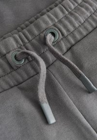 Los pantalones deportivos grises cuentan con una pretina texturizada con costuras fruncidas, dos ojales y un cordón con extremos de silicona a juego en gris.