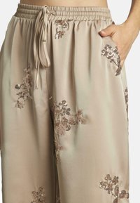 Pantalons satin beige clair avec une taille élastique, ornés de délicates embellissements de sequins floraux et de poches latérales.