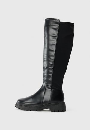 Bottes noires montantes en cuir lisse à l'avant et en tissu à l'arrière, avec une semelle en caoutchouc texturé et un bout arrondi.