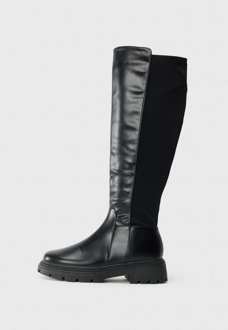Bottes noires montantes en cuir lisse à l'avant et en tissu à l'arrière, avec une semelle en caoutchouc texturé et un bout arrondi.