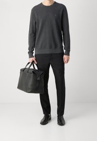 Maglione grigio scuro a girocollo, pantaloni neri e scarpe in pelle nera lucida. Tiene una borsa in pelle nera a trama con cinturini regolabili.