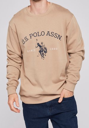 Beige sweatshirt made of soft fabric, featuring long sleeves and a crew neck. A dark graphic of polo players and text are centered on the front.