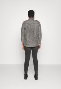 Grå långärmad skjorta med knäppt krage, kombinerad med mörkgrå leggings och svarta ankelboots, sedd bakifrån.