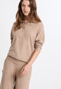 Beżowy sweter z kapturem i regulowanym sznurkiem, o luźnym kroju, z prążkowanymi mankietami i miękką teksturą. W komplecie ze spodnimi spodniami.