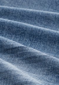 Modrý denim s texturovaným povrchem, zobrazující jasné linie z překládaných vrstev a mírný lesk zvýrazňující vlákna.