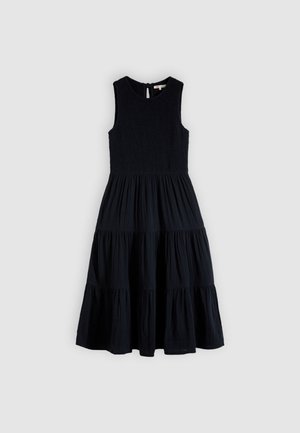 Robe midi noire sans manches avec corsage ajusté texturé et jupe à volants froncée suspendue devant un fond uni.