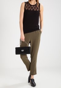 Haut sans manches noir avec des détails en dentelle, pantalon slim-fit vert olive, sac à main noir texturé avec quincaillerie argentée, et chaussures à talons noires.