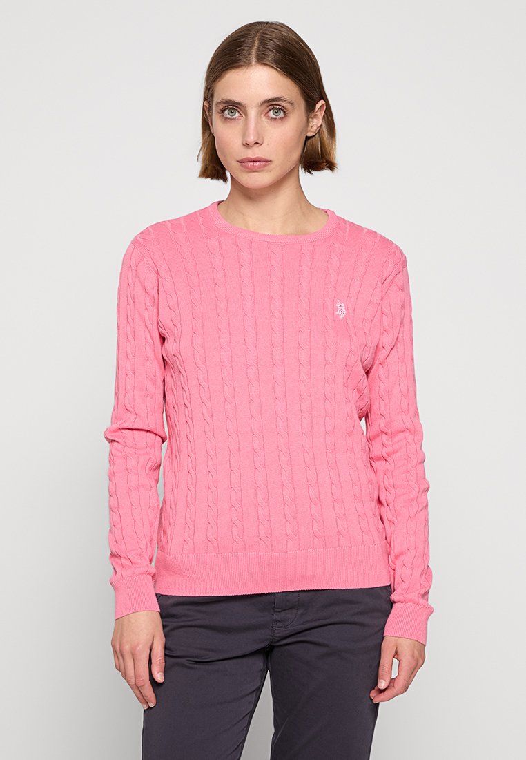 Rosa Kabelstrickpullover mit gerippten Bündchen und Saum. Lange Ärmel, runder Ausschnitt, mit einem kleinen Emblem auf der Brust. Weiche Textur.