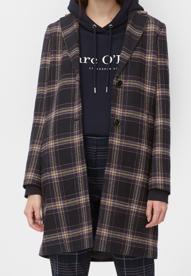 Femme portant un long manteau à carreaux foncé sur un sweat à capuche bleu marine avec un texte blanc et un pantalon à carreaux foncé assorti.