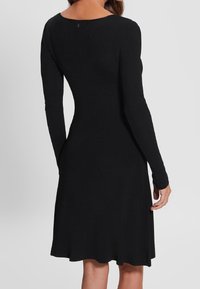 Robe noire à manches longues côtelées avec un dos échancré en forme de scoop, un corsage ajusté et un ourlet évasé. Le tissu semble lisse avec une texture douce.