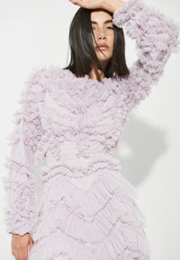 Lavendelklänning med lager av rynkig textur över hela, långt ärmar och en figurnära siluett, med ett slätt underliggande tyg.