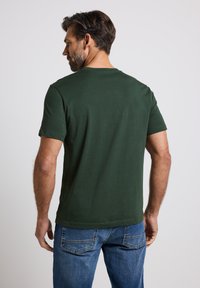 Groene T-shirt met korte mouwen in een klassieke pasvorm, van katoen, met ronde halslijn en eenvoudig ontwerp. Draag het met blauwe jeans, gezien vanuit de achterkant.