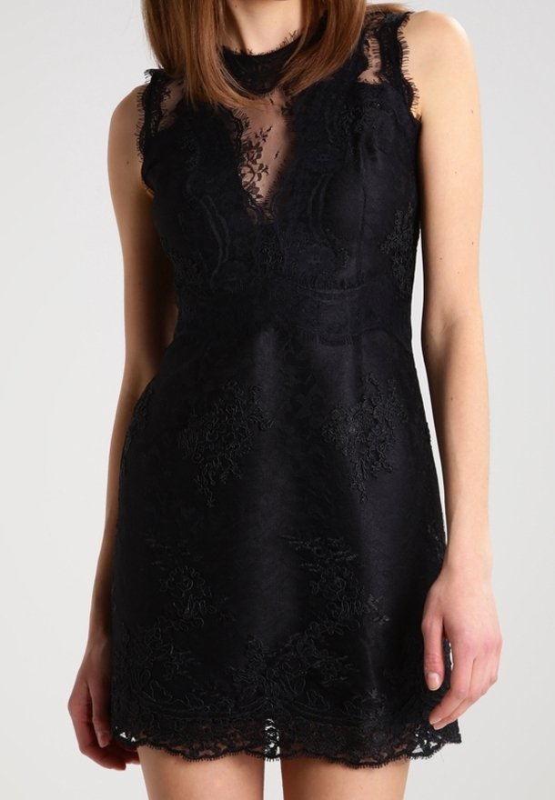 Robe mini noire sans manches en dentelle avec un décolleté en dentelle florale transparente et un ourlet festonné, portée par une personne debout aux cheveux bruns mi-longs.