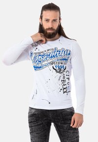 Langärmliges weißes T-Shirt mit blauer Grafikdruck, der Text und Spritzdesigns zeigt. Das Material scheint aus Baumwolle oder einem Baumwollgemisch zu sein.