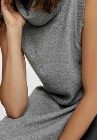 Grå stickad klänning utan ärmar med huva, gjord av mjukt, strukturerat material, med en lös passform och draperad design.