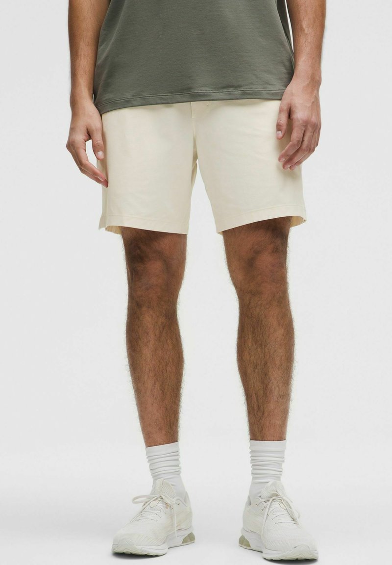 Șorturi din bumbac bej, cu croi dreapt, buzunare laterale și o croială relaxată. Purtați cu un tricou verde închis și pantofi sport albi.